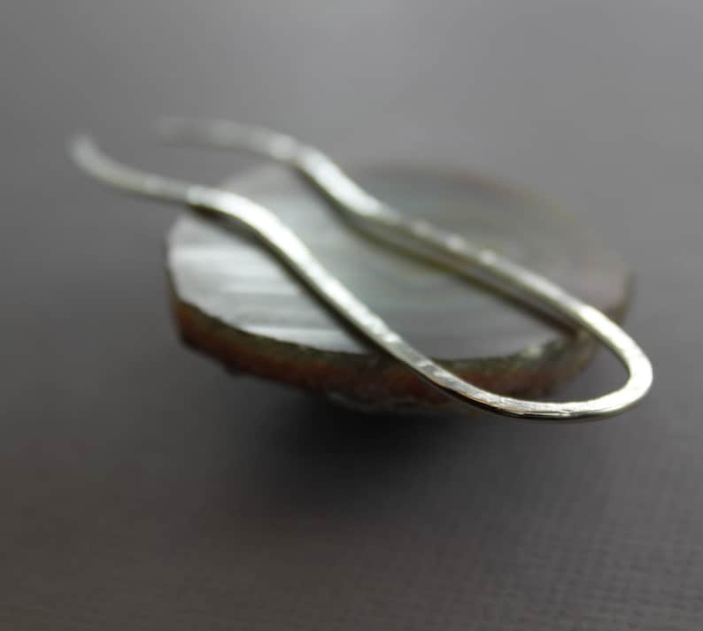 May include: A silver, hammered, open-ended loop earring. The earring is resting on a piece of agate.