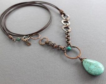 May include: A turquoise teardrop pendant necklace with a copper chain and leather cord. The pendant features a small turquoise bead and a copper wire wrapped around the teardrop.