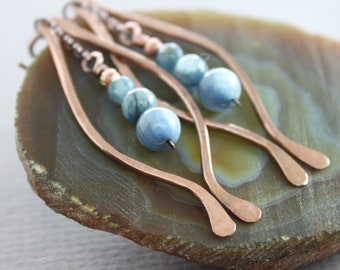 May include: A pair of copper wire earrings with blue gemstone beads. The earrings are shaped like a curved line and have a delicate, minimalist design.