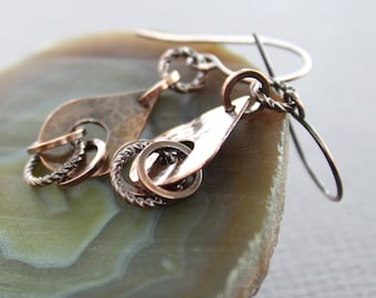 May include: A pair of copper earrings with a hammered finish and a twisted wire design. The earrings are hanging from a silver hook.