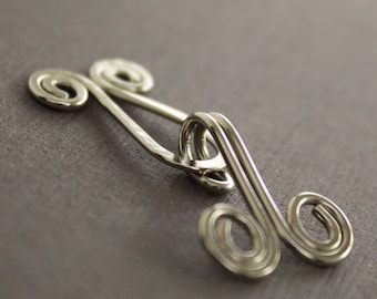 May include: Silver metal hook closure with a decorative swirl design. The hook is made of wire and has a smooth, polished finish.