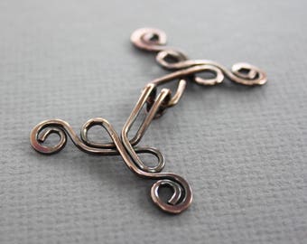 May include: A silver-toned metal clasp with a decorative design featuring multiple swirls and loops.