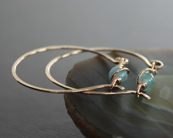 May include: Gold hoop earrings with a light blue gemstone wrapped in gold wire.