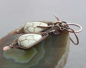 May include: A pair of copper wire wrapped earrings with white howlite stone drops. The earrings have a simple, elegant design.
