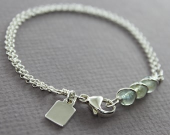 May include: A silver chain bracelet with a silver charm and light blue gemstone beads.