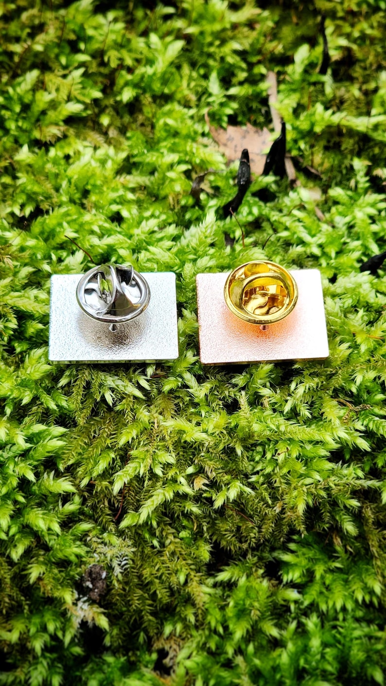 The backs of two rectangular pins with butterfly style clasps. One is silver and one is rose gold. The clasps are silver and gold respectively.