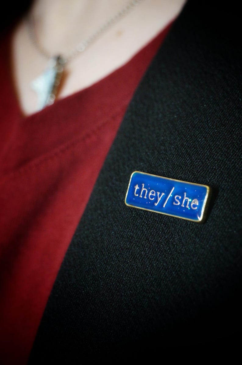 The they/she badge on a lapel. The background looks blue