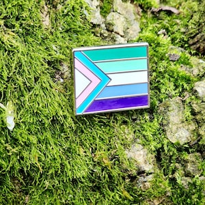 A rectangular hard enamel pin with the trans pride chevron from the progress pride flag on the left side. The rest of the design is the gay man pride stripes, outlined in silver metal.
