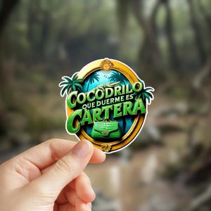 May include: A gold-framed sticker with a green crocodile sleeping inside a green purse. The text reads "Cocodrilo que duerme es cartera".