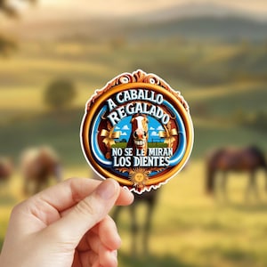 May include: A round sticker with a blue and gold border. The sticker features a cartoon horse with a toothy grin and the text "A CABALLO REGALADO NO SE LE MIRAN LOS DIENTES".