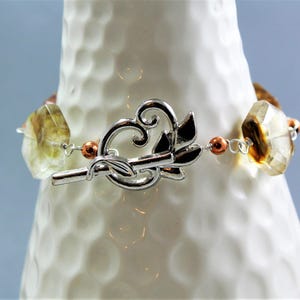 Pode incluir: Uma pulseira de pedras preciosas com fecho prateado. A pulseira apresenta pedras preciosas facetadas, castanho claro e amarelas, conectadas por fio de prata e pequenas contas cor de cobre. O fecho &eacute; um design prateado decorativo.