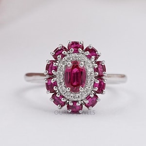 May include: A white gold ring with a large oval ruby surrounded by a halo of smaller rubies and diamonds. The ring has a floral design.