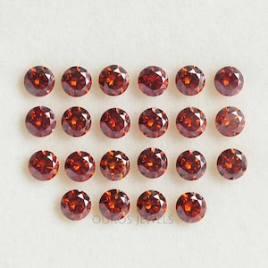 Puede incluir: Veinticuatro piedras preciosas redondas de color rojo dispuestas en forma de semic&iacute;rculo sobre una superficie blanca. Las piedras preciosas son todas del mismo tama&ntilde;o y forma, y tienen un ligero tono naranja.