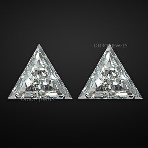 May include: Two clear triangular shaped gemstones with a faceted design. The gemstones are set against a black background.