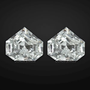 May include: Two loose, colorless, pentagon-shaped diamonds with a brilliant cut, featuring multiple facets that reflect light. Each stone displays a sharp, pointed top and a flat base, with the small text OUROS JEWELS printed at the bottom.