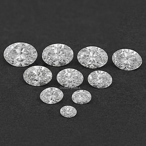 Pu&ograve; includere: Una collezione di gemme ovali, trasparenti e sfaccettate, disposte a forma di piramide su uno sfondo nero.