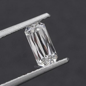 May include: A clear, rectangular emerald cut diamond gemstone held in tweezers. The diamond has a brilliant, faceted surface.