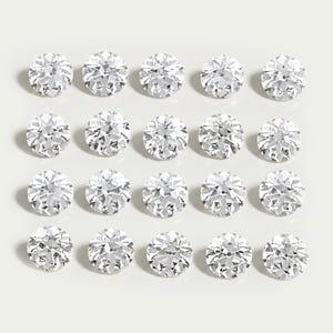 Puede incluir: Una colección de veinte piedras preciosas redondas, transparentes y facetadas, dispuestas en una cuadrícula de cuatro por cinco. Cada piedra presenta un corte brillante con múltiples facetas triangulares que reflejan la luz.