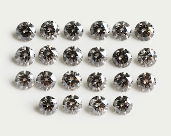 Könnte beinhalten: Eine Ansammlung von zweiundzwanzig runden, facettierten, dunkelgrauen Edelsteinen, die in vier Reihen angeordnet sind. Jeder Stein weist einen Brillantschliff mit mehreren reflektierenden Oberflächen auf, die ein funkelndes, metallisches Aussehen erzeugen.