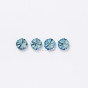 May include: Four round, faceted, light blue gemstones on a white background. The gemstones are arranged in a row.