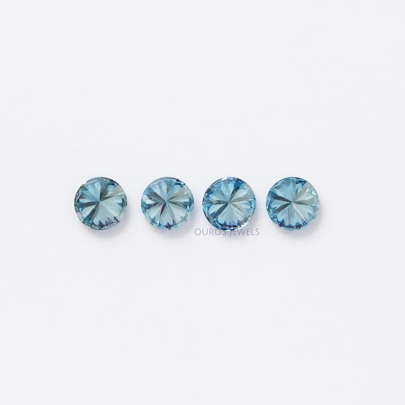 May include: Four round, faceted, light blue gemstones on a white background. The gemstones are arranged in a row.
