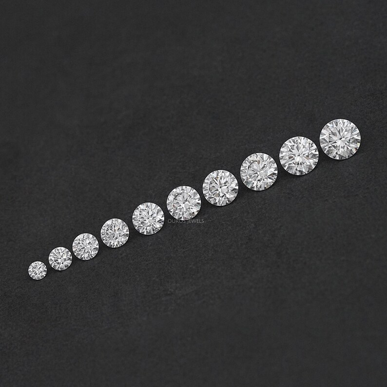 May include: A row of ten round, clear, faceted gemstones of varying sizes, arranged from smallest to largest on a black surface.