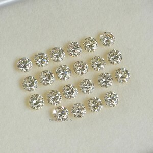 May include: A collection of 20 round, clear, faceted gemstones. The gemstones are arranged in a circular pattern on a white surface.