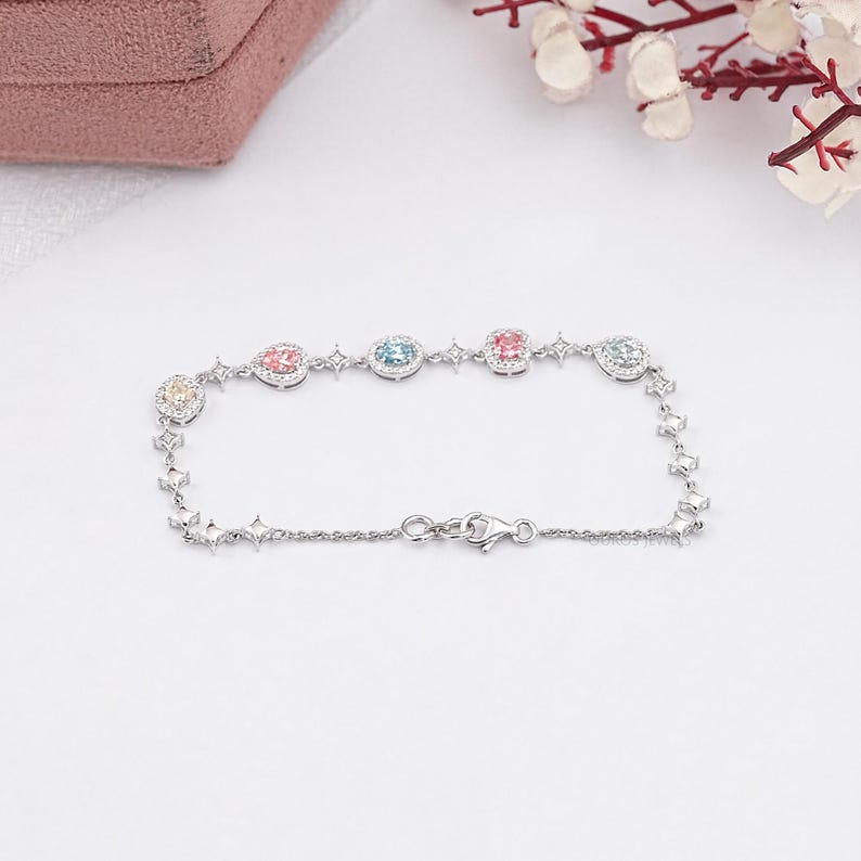 Puede incluir: Un brazalete de plata con una cadena delicada y cinco piedras preciosas de colores. Cada piedra preciosa est&aacute; rodeada de piedras m&aacute;s peque&ntilde;as y transparentes.