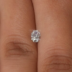May include: A faceted, oval-shaped diamond with a brilliant cut. The diamond is clear and colorless, reflecting light. The text "OUROS JEWELS" is visible.
