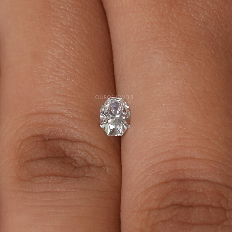 May include: A faceted, oval-shaped diamond with a brilliant cut. The diamond is clear and colorless, reflecting light. The text "OUROS JEWELS" is visible.