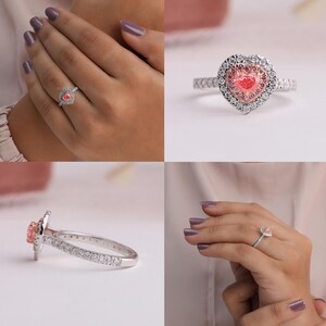 May include: A heart-shaped ring featuring a central pink stone surrounded by a halo of smaller pink stones and an outer border of clear white stones. The band is silver-toned and encrusted with small clear white stones along the shank.