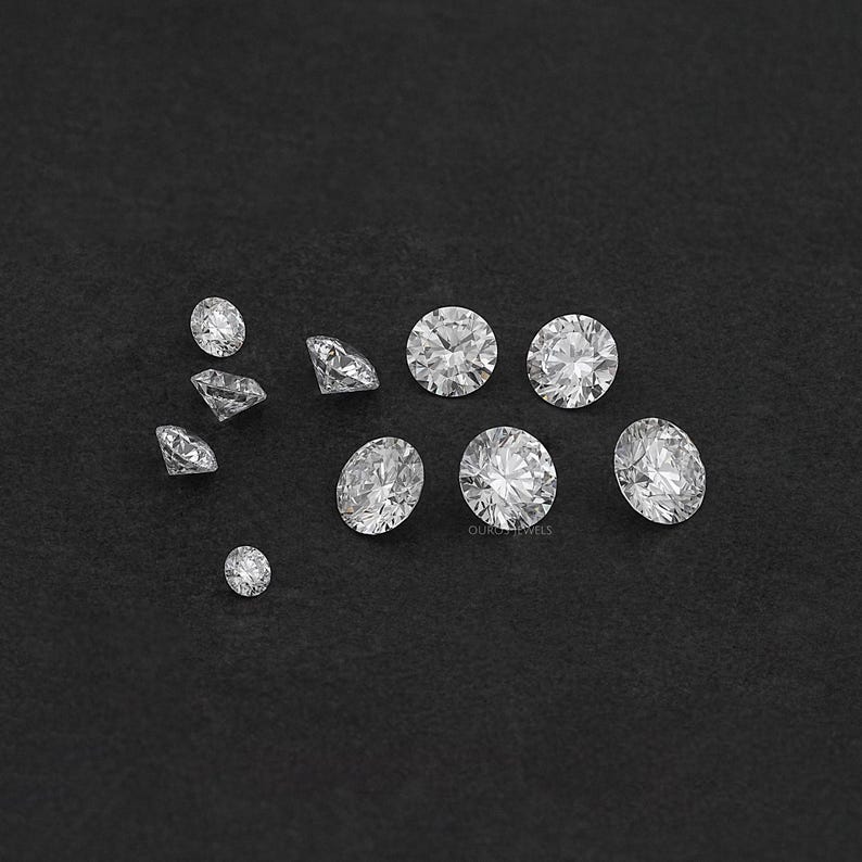 May include: A collection of round, clear, faceted gemstones of various sizes on a black background.