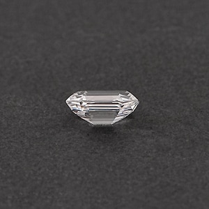 May include: A clear, rectangular emerald cut gemstone with a slight shimmer.