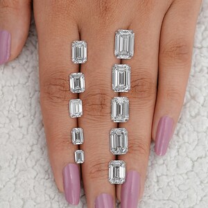 May include: A set of eight emerald cut diamonds of varying sizes, displayed on a hand. The diamonds are clear and brilliant.