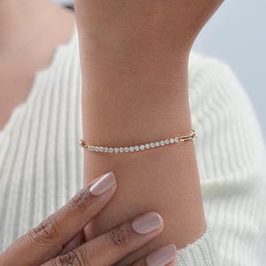 Pu&ograve; includere: Un braccialetto dorato con una fila di piccole pietre scintillanti. Il braccialetto &egrave; allacciato a un polso, mettendo in risalto il design delicato e la brillantezza delle pietre. Il braccialetto &egrave; un gioiello.