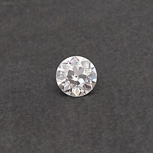 May include: A round, clear, faceted diamond gemstone on a gray background.