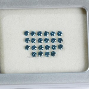 May include: A collection of 20 round, blue gemstones displayed in a white tray. The gemstones are arranged in a rectangular shape with the text "OUROS JEWELS" printed below.