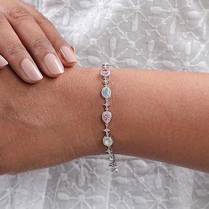 Puede incluir: Un brazalete de plata con una cadena delicada y piedras preciosas de colores. Las piedras preciosas est&aacute;n engastadas en un halo de diamantes m&aacute;s peque&ntilde;os. El brazalete es una pieza de joyer&iacute;a hermosa y elegante.