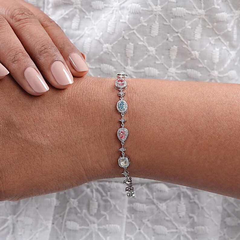 Puede incluir: Un brazalete de plata con una cadena delicada y piedras preciosas de colores. Las piedras preciosas est&aacute;n engastadas en un halo de diamantes m&aacute;s peque&ntilde;os. El brazalete es una pieza de joyer&iacute;a hermosa y elegante.