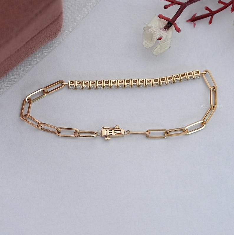 Pu&ograve; includere: Un braccialetto d'oro con un design a catena a maglie rettangolari. Il braccialetto presenta una fila di piccole pietre trasparenti disposte in linea retta. La chiusura &egrave; un design rettangolare e sicuro. Il braccialetto &egrave; esposto su una superficie chiara.
