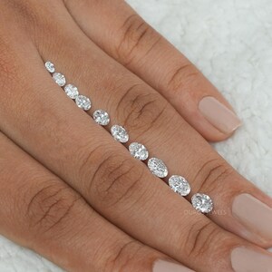 May include: A row of oval-shaped diamonds of varying sizes, arranged from smallest to largest, on a person's finger.