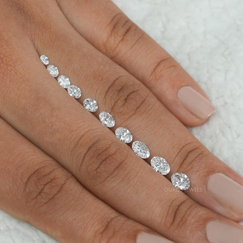 May include: A row of oval-shaped diamonds of varying sizes, arranged from smallest to largest, on a person's finger.