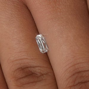 May include: A clear emerald cut diamond gemstone on a finger.