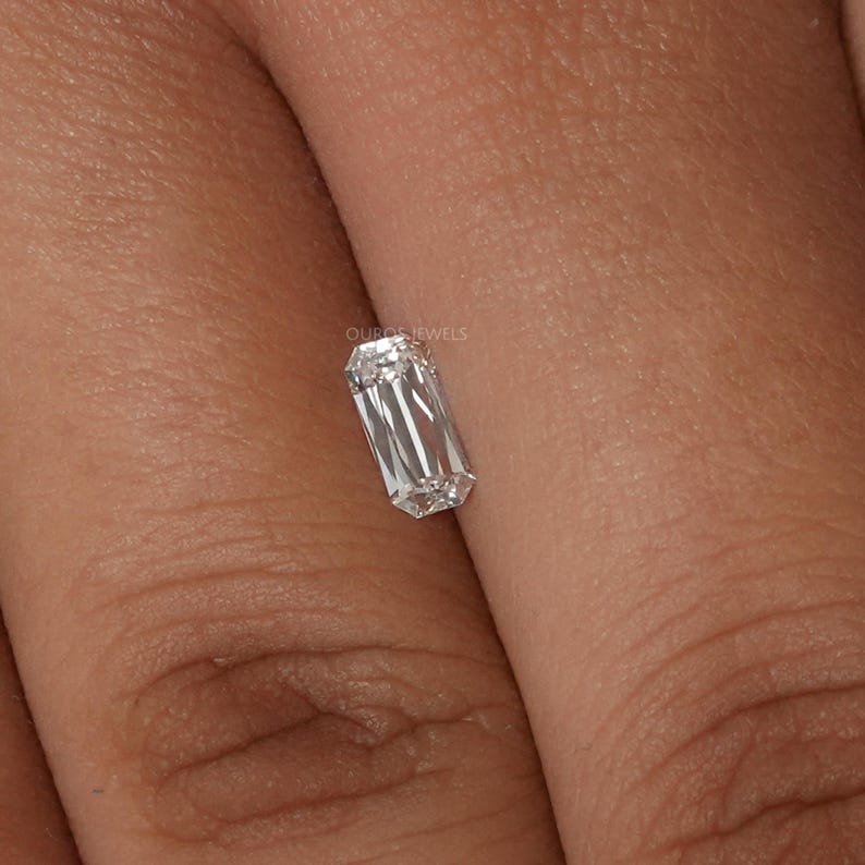 May include: A clear emerald cut diamond gemstone on a finger.