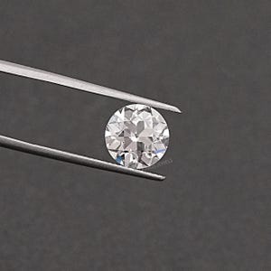 May include: A clear round gemstone with facets, held by tweezers against a gray background.