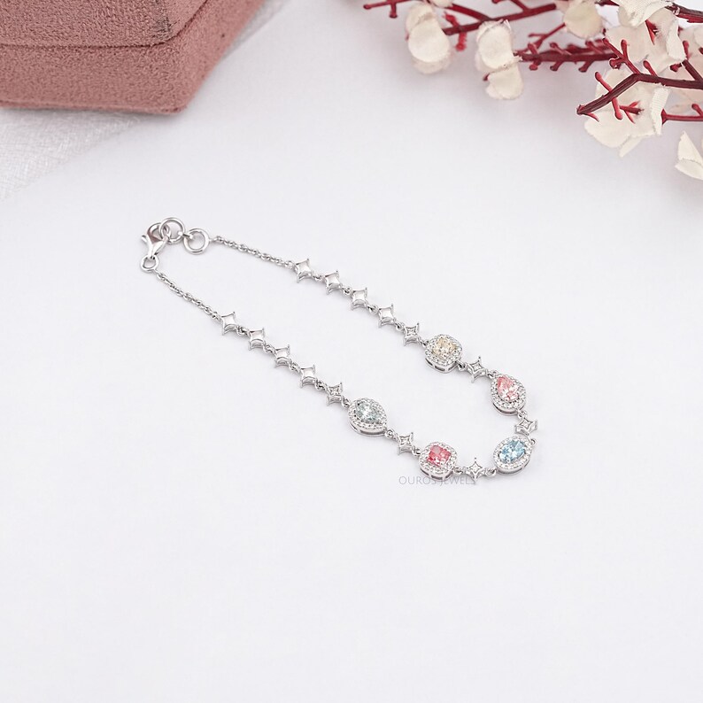 Puede incluir: Un brazalete de plata con una cadena delicada y cinco piedras preciosas de colores engastadas en un marco de plata. Las piedras preciosas son rosa, amarillo, azul y verde.