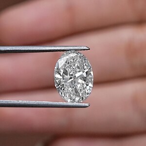 Pu&ograve; includere: Un diamante trasparente di forma ovale, tenuto da una pinzetta. Il diamante &egrave; sfaccettato e riflette la luce.