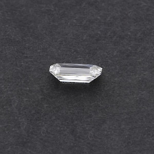 May include: A clear, rectangular emerald cut diamond gemstone on a black background.