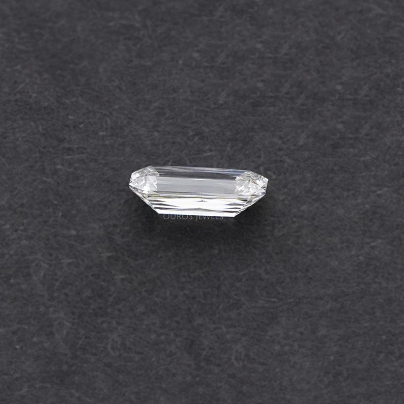 May include: A clear, rectangular emerald cut diamond gemstone on a black background.