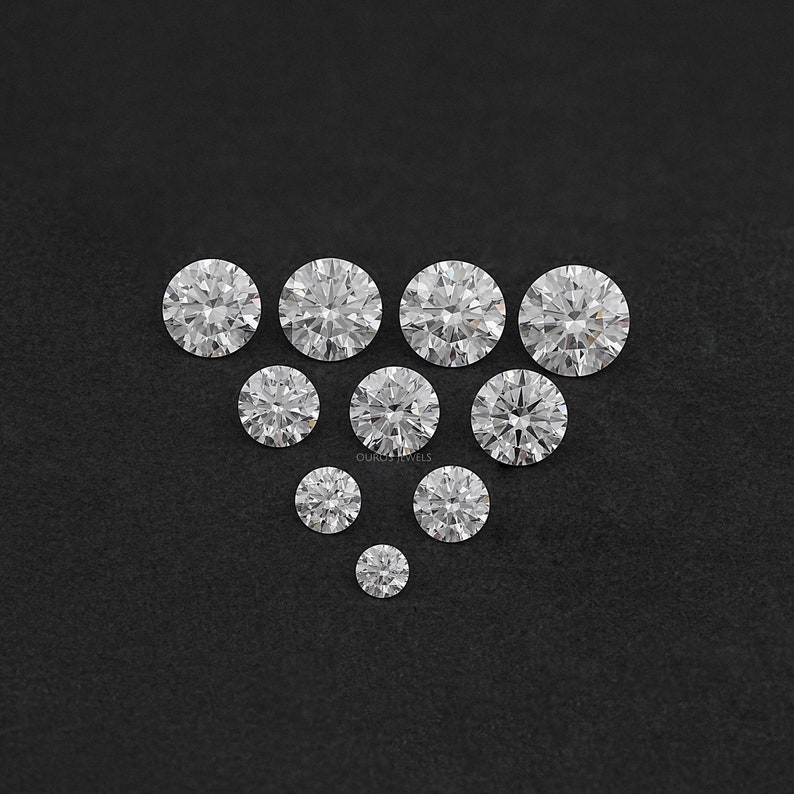 May include: A collection of round, clear, faceted gemstones arranged in a pyramid shape on a black background.